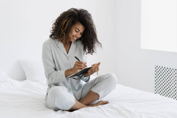 young afro american woman writing in personal journal - pen color image black book imagens e fotografias de stock