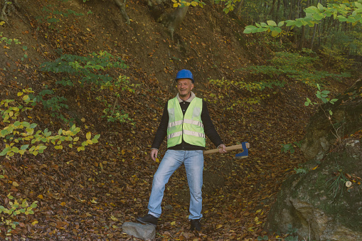Adult man lumberjack worker carry axe and wearing protective work helmet and reflective cloth in forest
