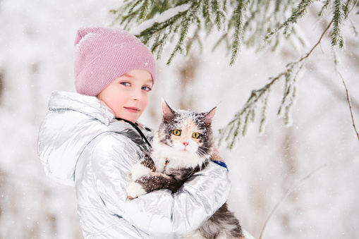 little girl carries a cat in her arms in a snowy winter