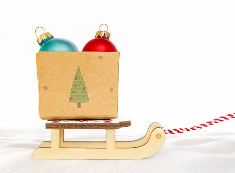 a box with a Christmas tree ornament stands on a sled on a white background