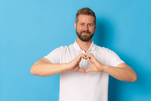 istock Young handsome man making heart figure with hands isolated over blue background. 1348654891