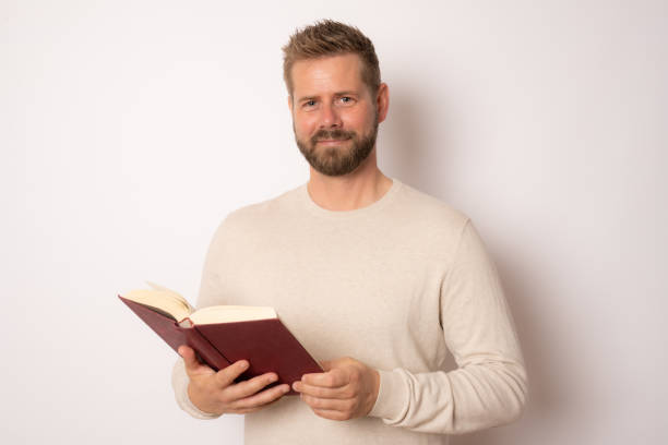 istock Handsome young man reading a book isolated over white background. 1348655005