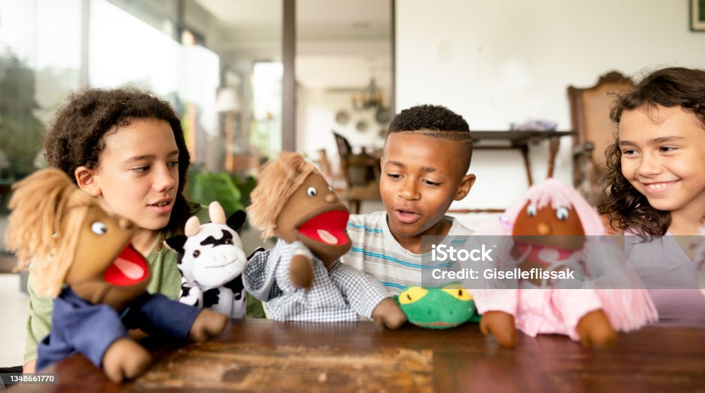 Smiling children putting on a play together with hand puppets Diverse group of young children smiling while putting on a play with hand puppets at a friend's home Puppet Stock Photo