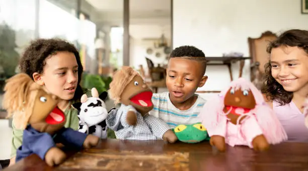 Diverse group of young children smiling while putting on a play with hand puppets at a friend's home