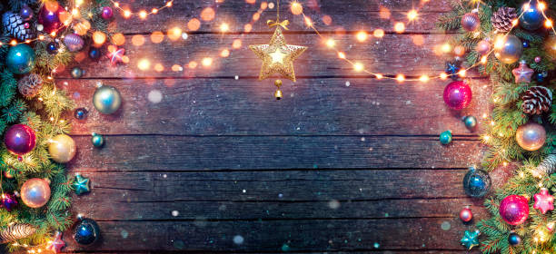 istock Christmas Decoration With Fir Branches And Baubles Illuminated With String Lights On Dark Wooden Table With Abstract Snowfall 1348668115