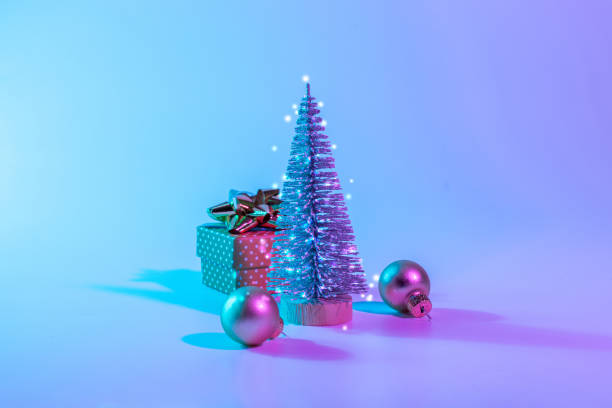 istock Neon Christmas winter background. Minimal abstract tree, xmas gift box. Holiday decoration bauble ball on neon gradient backdrop. Happy new year copy space. 1348671406