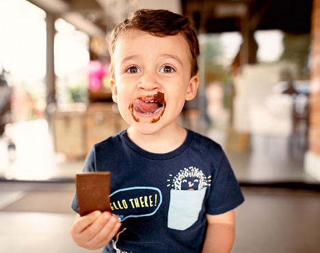 Portrait of a cute little boy smiling while standing in his home and licking melted chocolate from his face