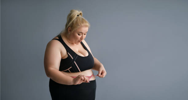 若い肥満の女性は、巻尺で腰を測定します。 - 1インチ ストックフォトと画像