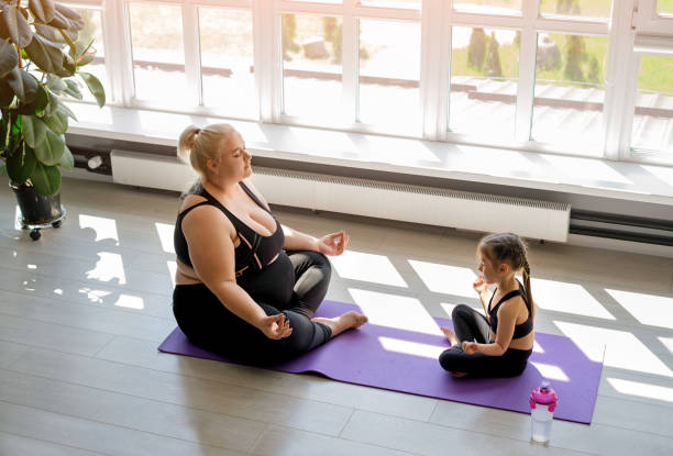 obese woman with daughter doing yoga, meditation in lotus position - child obesity imagens e fotografias de stock