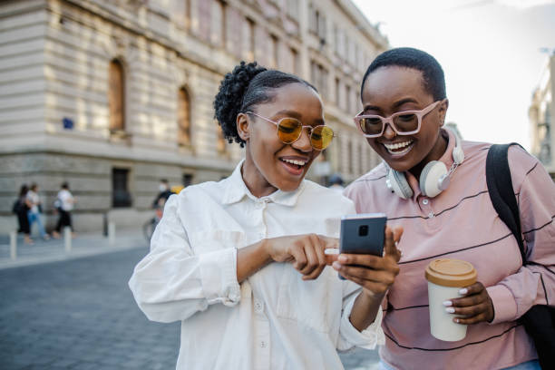 Two woman in the city, looking at the phone and smiling Two young woman standing on the street and looking at the phone generation z stock pictures, royalty-free photos & images