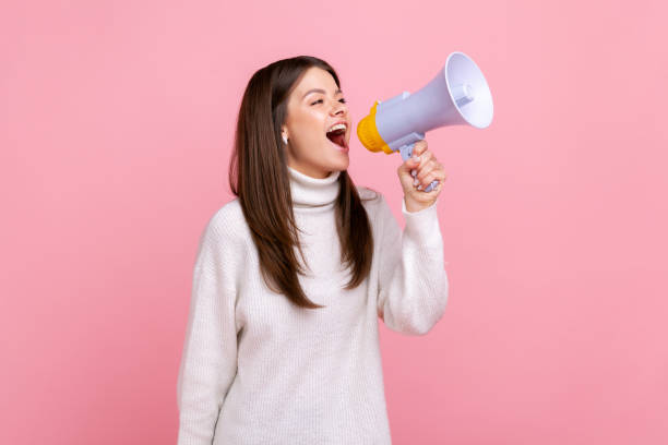 ritratto con vista laterale di una ragazza piuttosto positiva che urla al megafono, annunciando informazioni importanti. - strillare foto e immagini stock