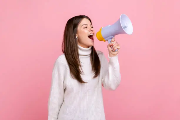 Photo of Side view portrait of pretty positive girl screaming in megaphone, announcing important information.