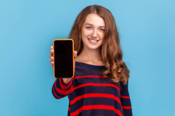 istock Woman showing smart phone with empty display for advertisement, looking at camera with happy face. 1348687576