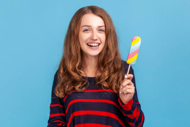 istock Woman holding rainbow ice cream, looking at camera with positive expression, feels hungry. 1348687901
