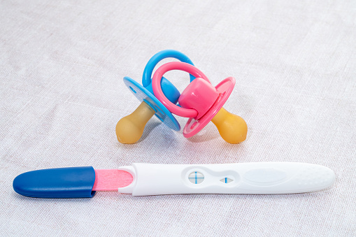 A pregnancy test stick showing a positive result with a pink and blue pacifier