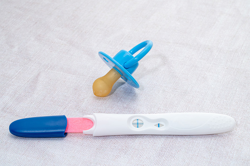 A pregnancy test stick showing a positive result with a blue pacifier