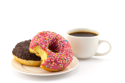 Still life with bitten colorful donut on plate and cup of black coffee isolated on a white background. Concept background of world problem of obesity and unhealthy nutrition