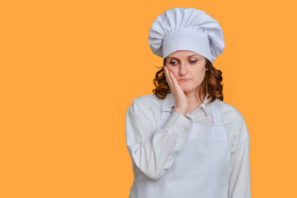 istock Sad woman chef holding her head on yellow studio background, copy space 1348717006