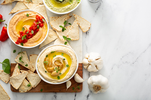 Hummus board with garlic, roasted red pepper and basil variety, served with pita overhead view