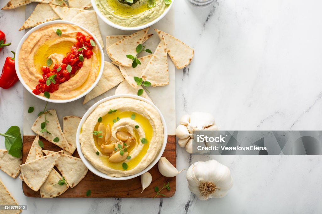 Hummus board with pita Hummus board with garlic, roasted red pepper and basil variety, served with pita overhead view Hummus - Food Stock Photo