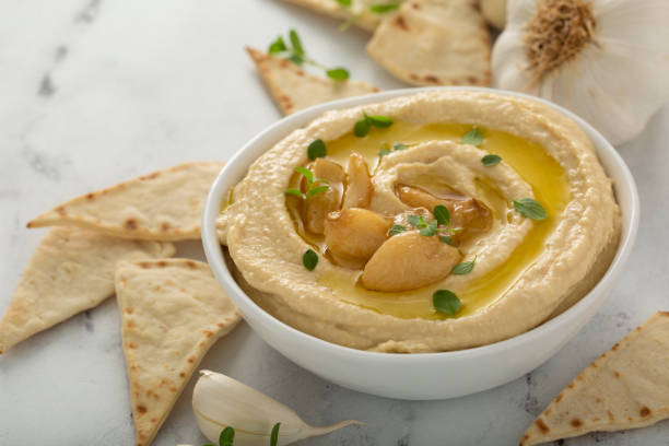 Roasted garlic hummus topped with olive oil Roasted garlic hummus topped with olive oil and garlic cloves hummus stock pictures, royalty-free photos & images