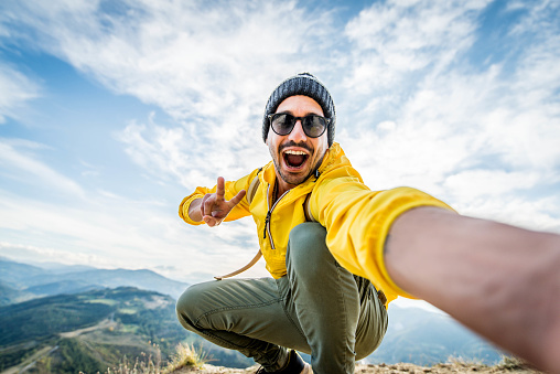 Joven excursionista tomando selfie retrato en la cima de la montaña - Chico feliz sonriendo a la cámara - Senderismo y escalada acantilado photo
