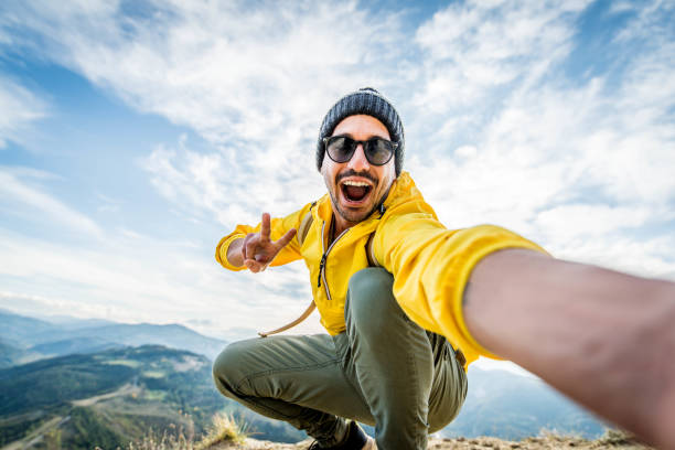 山の頂上で自分撮りの肖像画を撮る若いハイカーの男 - カメラで微笑む幸せな男 - ハイキングと登山崖 - ブログ ストックフォトと画像