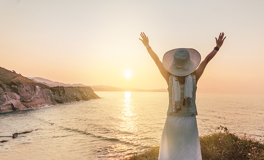 a woman with her arms raised, receives a sunset over the sea. in harmony with nature. ecology and environment concept.