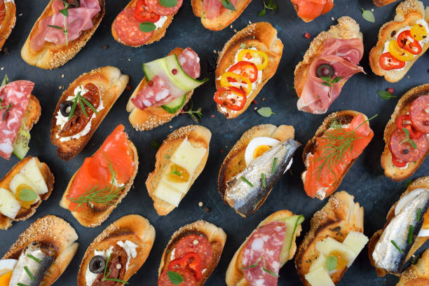 Colorful Spanish tapas Delicious mixed Spanish tapas with typical specialties on roasted baguette with sesame on a dark background tapas photos stock pictures, royalty-free photos & images