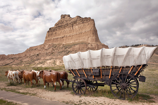 Clouds pass over a frozen oxen team pulling a Conestoga Wagon on the Oregon Trail with Scotts Bluff in the background in Scotts Bluff National Monument in Nebraska.