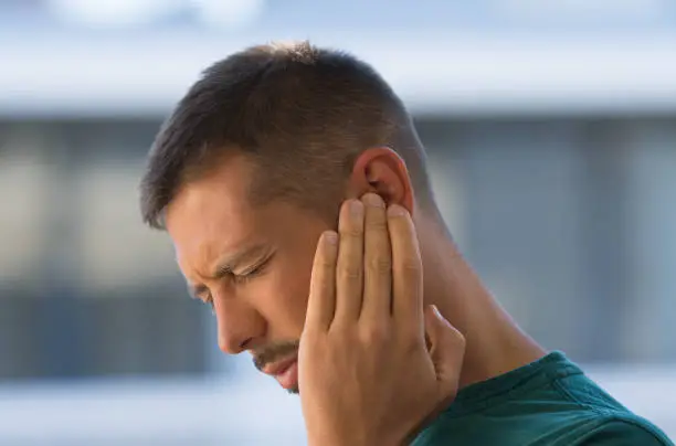 Young man with earache, otitis or tinnitus. Ear inflammation. Man suffering from ear pain. High quality photo