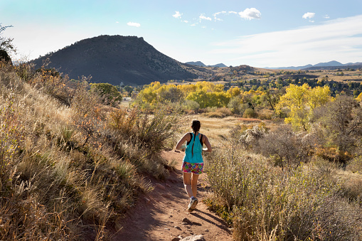 Winding through sandstone cliffs with autumn colors, a woman with a ponytail trail runs in the morning on the Trading Post Trail in Red Rocks Park in the Front Range Rocky Mountains Colorado.