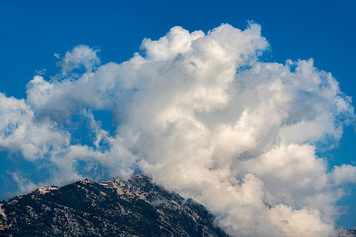 Cloudscape on top of the mountain in blue sky. The name of this visible mountain is Babadag and it is located in Fethiye, Turkey. The altitude of the summit is 1,969 meters.