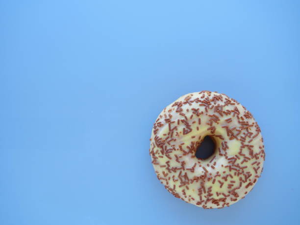 istock Doughnut close-up on blue background. Delicious cake covered with vanilla icing and chocolate sprinkles. High-calorie breakfast or snack. Sweet dessert with vanilla and chocolate, donut or dough. 1348768261