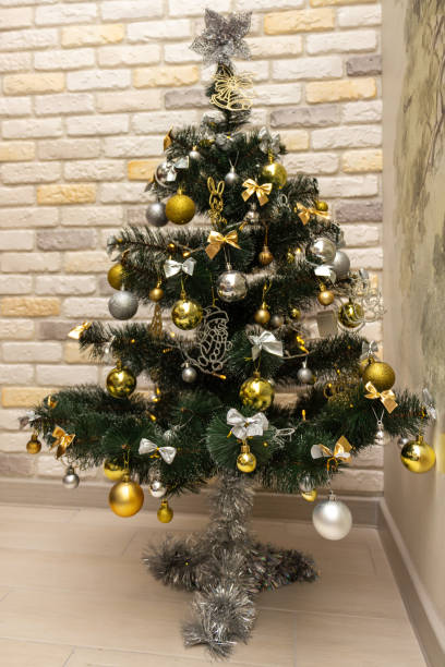 istock Decorated Christmas tree with the gold and silver baubles, multi-colored bows, animals, bells, lit garlands against the decorative brick wall background. Winter holidays concept 1348769257