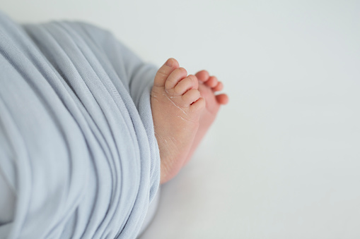 Newborn feet wrapped in a light purple blanket. Front view. Copy space.