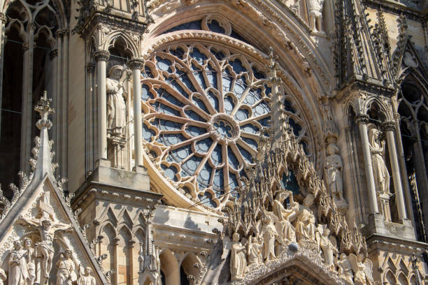 This image shows the ornate High Gothic exterior architecture of the Our Lady of Reims Cathedral in Reims, France, with view of the central round rose window. Officially known as the Notre-Dame de Reims.