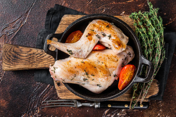 istock Fried rabbit legs in a pan with herbs. Dark background. Top view 1348797660