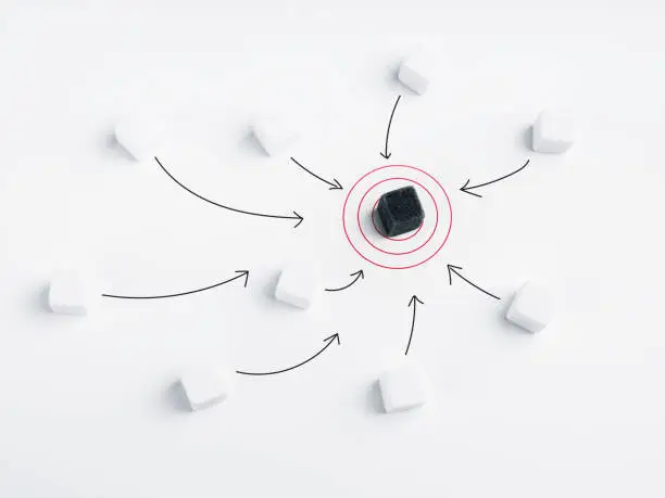 Photo of The black dice at the center of the red target. The white dice with arrows heading towards the same target, black dice on white background. Goals, difference, influencer, unique leadership concept.
