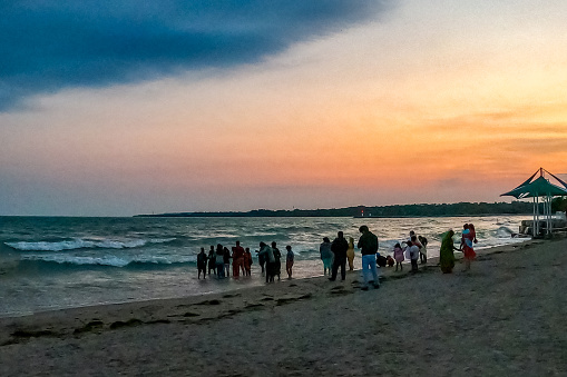 A group of oriental people are doing a baptism ceremony for a young child at beach of  Beachfront Park at dusk, Ontario, Canada.