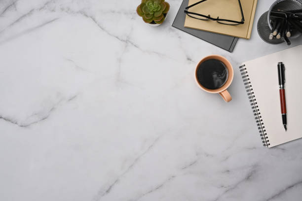 istock Stylish workspace with cup of coffee, notebooks and glasses on marble table. Top view. 1348828453
