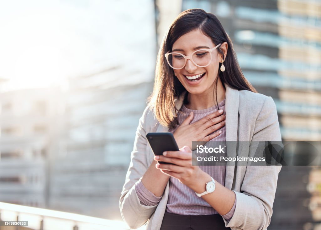 Shot of an attractive young businesswoman standing alone outside and looking surprised while using her cellphone I just got the best review from a client Happiness Stock Photo
