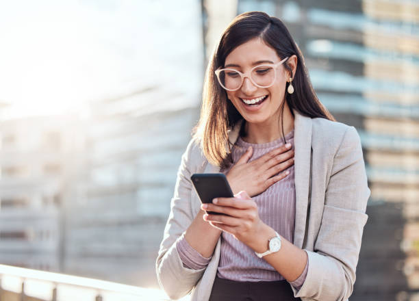 shot of an attractive young businesswoman standing alone outside and looking surprised while using her cellphone - disbelief imagens e fotografias de stock