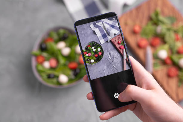 istock Man shooting fresh vegetable salad with mozzarella and spinach on cell phone camera. Cooking, blogging and healthy eating concept. 1348832781