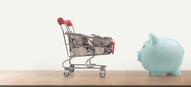 Toy shopping cart with coins and Piggy bank. Consumer society trend