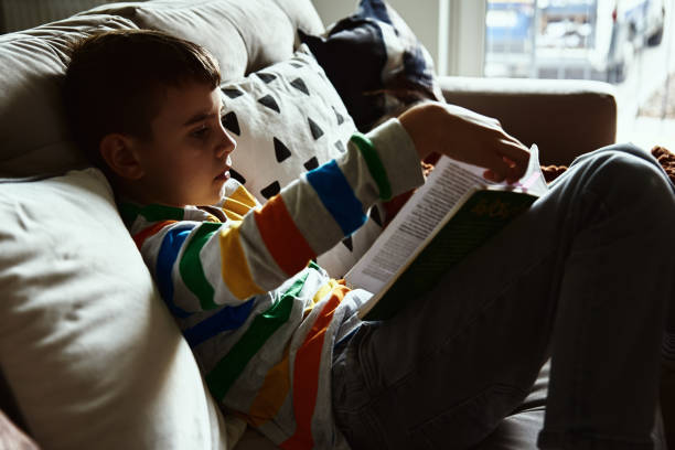 istock Child boy reading book on the sofa at home 1348833545