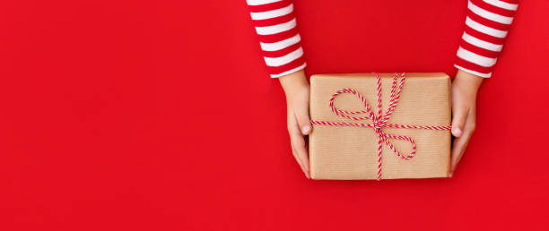 istock gift box in children's hands on a red background, presenting a gift, christmas background 1348835968