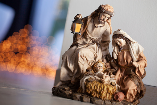 Old Christmas nativity set, with Joseph, Mary, and the baby Christ child in a manger. Christmas tree on the background.