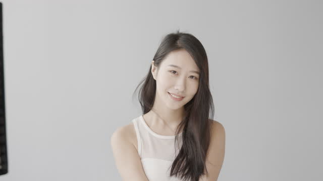 A gentle and beautiful asian woman wearing a white coat shoots a video in the studio. The wind blows through her long black hair and looks forward with a smile