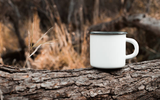 istock Camping metal white mug mockup standing on tree in forest outdoors, copy space for text. Enamelled empty cup for branding or logo 1348836687